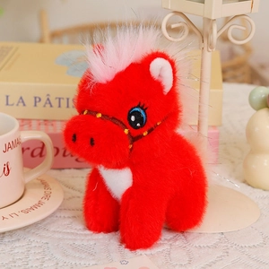 Close-up of a red plush horse keychain with white mane in a cozy tabletop setting