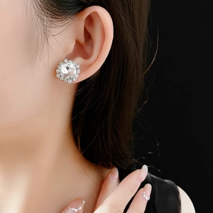 Close-up of sparkling crystal flower stud earring worn by model on black background