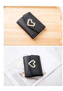 Detail of black short leather wallet featuring a gold heart clasp on a textured surface