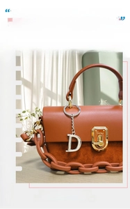 Detail of the brown leather shoulder bag with gold metal buckle and silver letter D charm