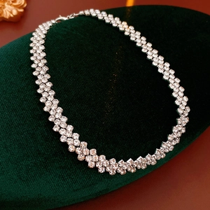 Macro detail of silver-toned rhinestone choker necklace on deep green velvet display stand