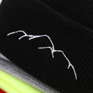 Black knit beanie with mountain peak embroidery and stacked colorful hats in background