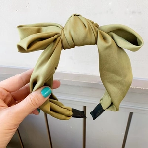 Detail of a grass green satin oversized bow headband with a smooth silk-like texture