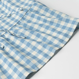 Close-up detail of blue and white gingham fabric with ruffled edges and drawstring design