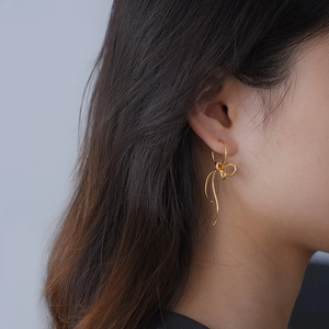 Close-up of elegant gold ribbon bow drop earrings worn by a model in soft lighting