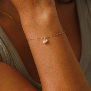 Detail eines eleganten 14K vergoldeten Armbands mit zwei weißen Perlenanhängern am Handgelenk
