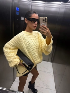 Detail of light yellow chunky cable knit sweater showing oversized fit and thick texture
