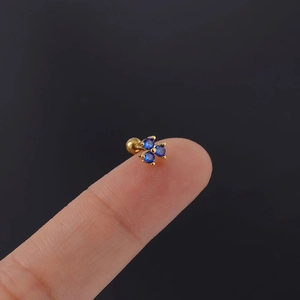 Close-up of golden stud earring with three blue zircons and screw ball back on fingertip