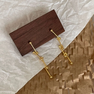 Macro detail of long gold drop earrings with metallic beads hanging on walnut wood