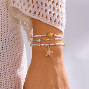 Three-layer beaded bracelet featuring gold starfish and shell charms on model wrist