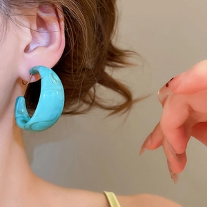 Detail shot of C-shaped teal marble acrylic hoop earrings with gold needle on model