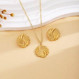 Golden spiral vortex necklace and earrings set displayed on a beige textured background