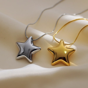 Polished silver and gold star pendants on snake chains over elegant beige silk fabric