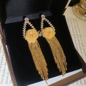 Detailed close-up of gold rose flower earrings with cascading tassels on black velvet box