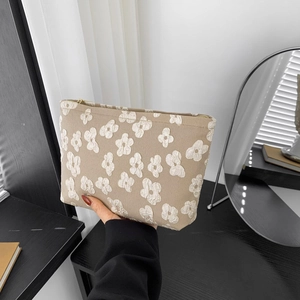 Beige cosmetic bag with 3D white floral texture and gold zipper held by hand