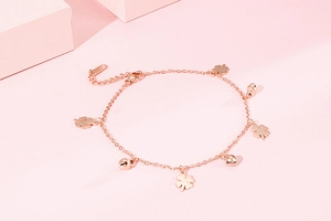 Detail of rose gold clover and bell anklet on a soft pink geometric background