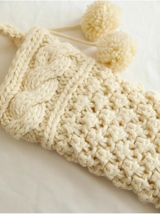 Close-up of cream knit Christmas stocking with thick cable pattern and soft pom-poms