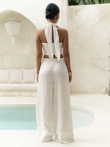 Detail of backless halter top with large bow and flowing beige linen wide-leg trousers
