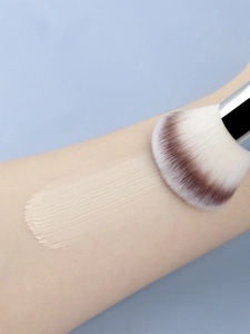 Macro detail of dense synthetic bristles applying liquid foundation on arm skin