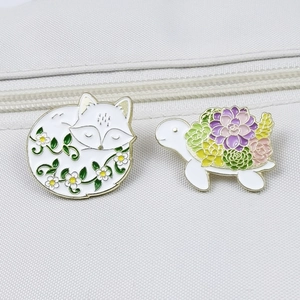 Detail of white fox and turtle enamel pins with floral and succulent patterns on fabric