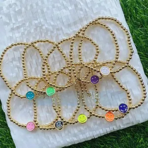 Close-up of golden beaded bracelets featuring colorful enamel smiley face charms