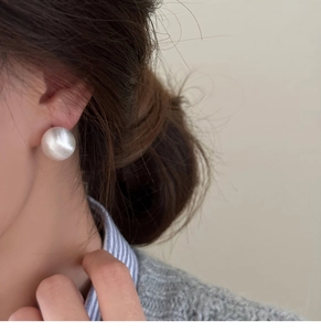 Close-up of minimalist silver spherical stud earring with brushed texture on model