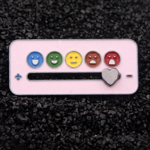 Macro shot of rectangular mood tracker pin with colorful emoji icons and heart slider