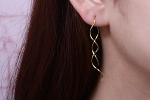 Detailed view of elegant gold spiral drop earrings featuring wave curves on female model