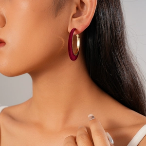 Macro detail of wine red velvet textured hoop earring worn by a model on plain background
