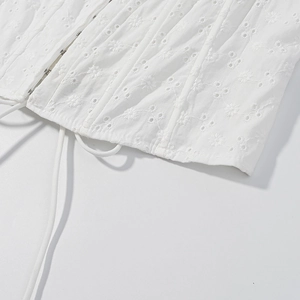 Dettaglio di top in cotone bianco con ricami floreali e chiusura con bottoni in metallo