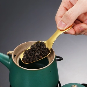 Golden 304 stainless steel tea scoop pouring loose leaf tea into a green teapot