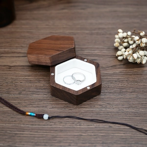 Macro detail of hexagonal black walnut ring box with white velvet lining and rings