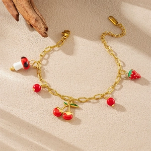 Bracelet chic en acier doré avec des charms cerise et champignon sur une surface beige