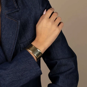 Close-up of a wide polished gold cuff bracelet on a model wearing a navy blazer