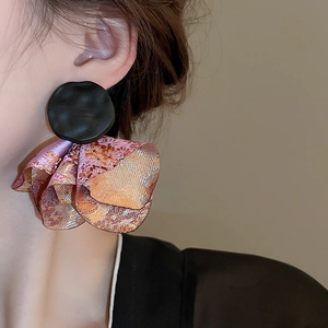 Close-up of model wearing matte black floral earrings with orange lace fabric details