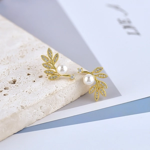 Elegant gold leaf pearl earrings with sparkling zircons on a white textured stone surface