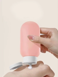 Applying white lotion from a pink silicone squeeze bottle for travel onto skin surface