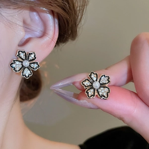 Vintage flower earrings with black enamel, crystals, and pearls in a hand-held shot