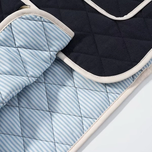 Close-up of diamond-quilted jacket fabric with navy and striped patterns and contrast piping