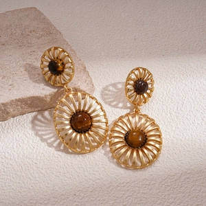 Retro hollow golden earrings with tiger eye stone on natural stone and beige background