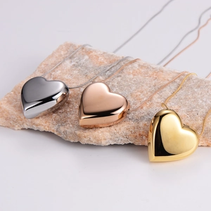 Three minimalist heart pendant necklaces in gold, silver, and rose gold on a stone base