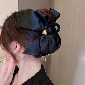 Détail d'une grande pince à cheveux nœud en satin noir avec cœur doré sur le modèle