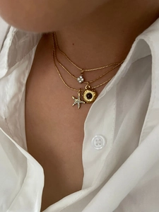 Detail of layered gold necklaces with starfish, sun, and floral charms on a model