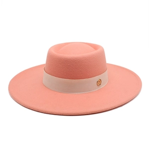 Detailed side view of coral pink wool fedora with beige ribbon and golden metal logo