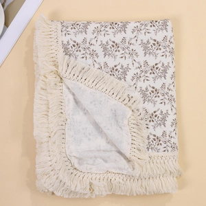 Detail of floral muslin baby blanket with woven tassels and soft cotton texture