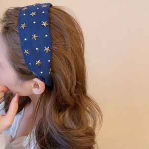 Détail d'un serre-tête en tissu bleu marine à étoiles dorées sur cheveux bruns