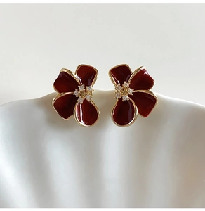 Détail macro de boucles d'oreilles fleur rouge foncé avec bords dorés 18K et cristal central