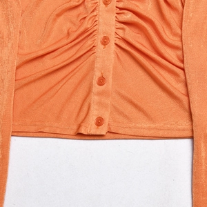 Close-up of orange pleated cardigan showing button closure and textured fabric detail