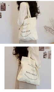 Detailed view of cream canvas tote bag featuring black typography print on shoulder strap