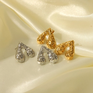 Détail macro de boucles d'oreilles dorées et argentées martelées sur du satin jaune